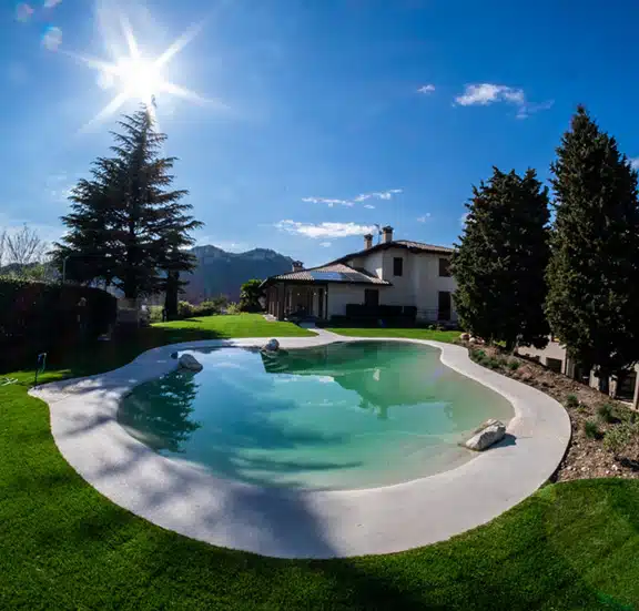 A small Biodesign pool with an umbrella and lounge seats surrounded by trees